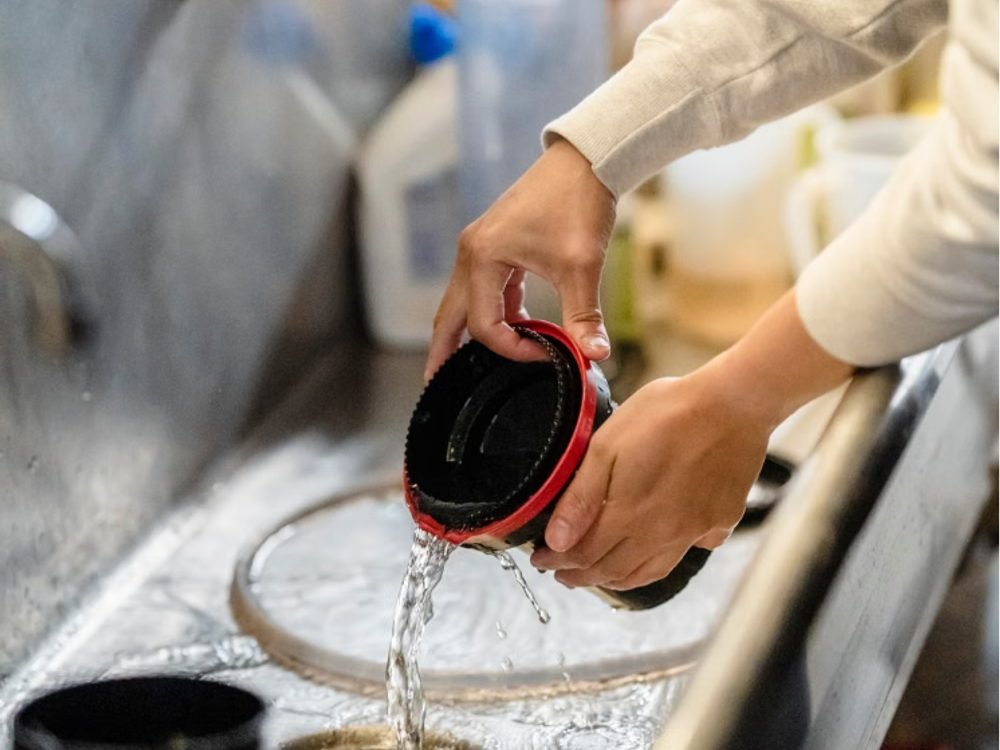 Close-up of a humidifier water tank being emptied and rinsed in a sink to prevent mold and bacteria buildup