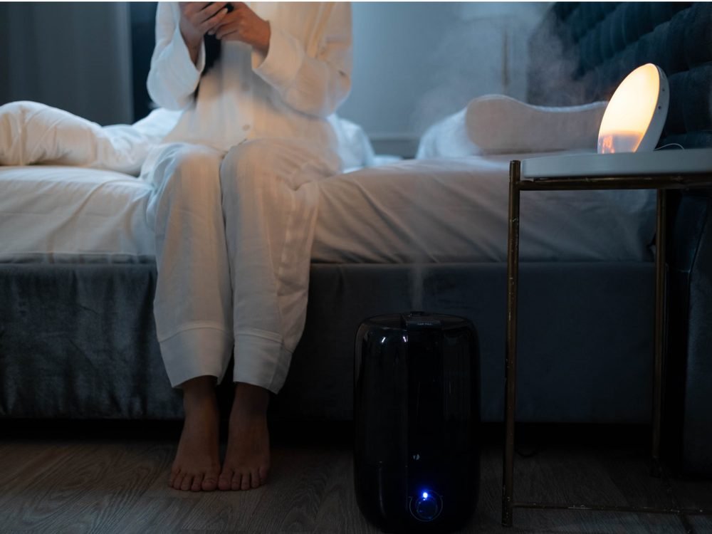 Side-by-side comparison of a cool mist humidifier and a warm mist humidifier releasing vapor in a bedroom